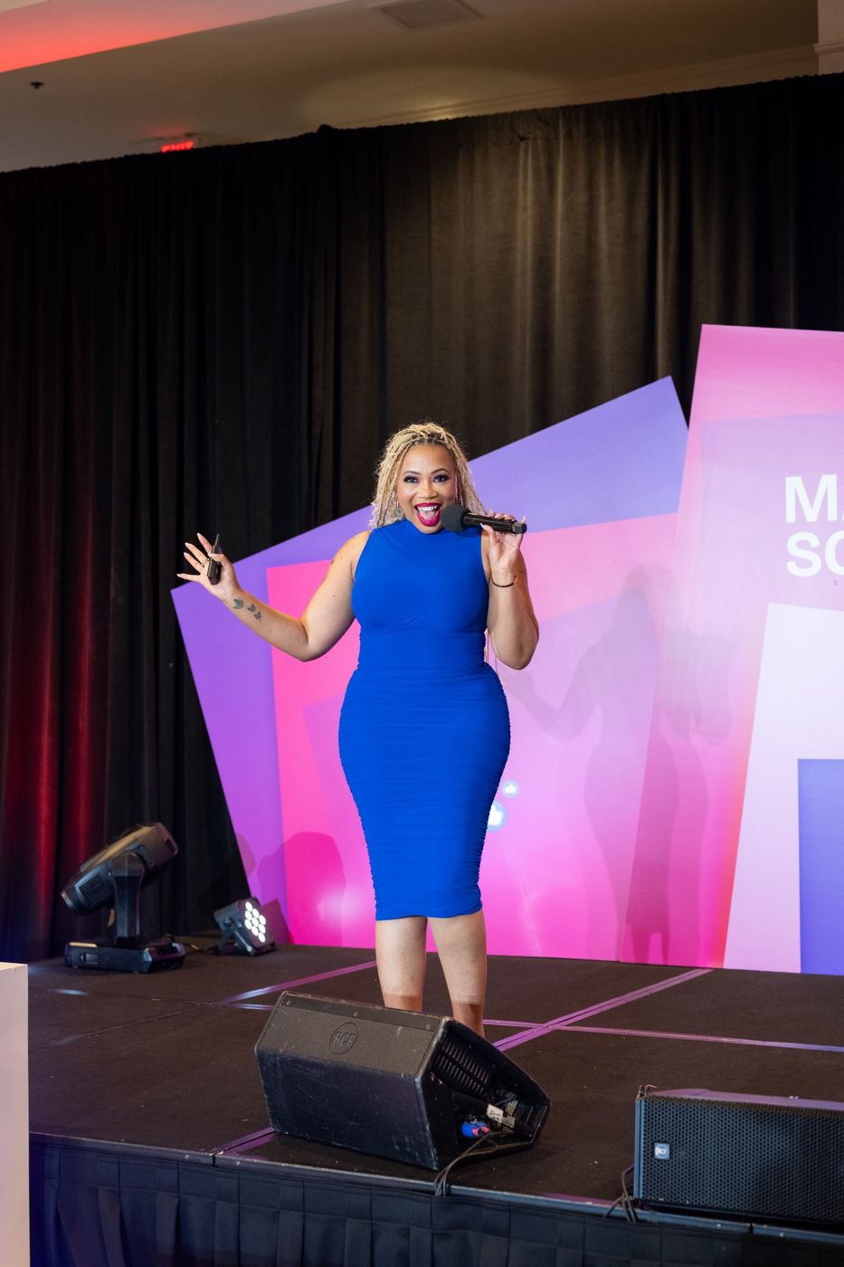 Aprille on stage at Marketing School LIVE with a microphone, mid-laugh